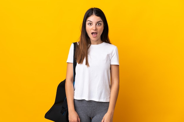 Young sport woman with sport bag isolated on yellow wall with surprise facial expression
