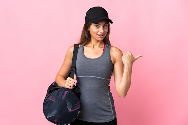 Young sport woman with sport bag on pink pointing to the side to present a product