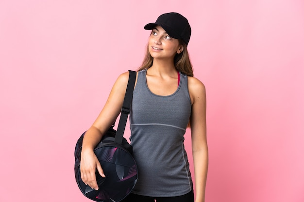 Молодая спортивная женщина со спортивной сумкой на розовом, думая об идее, глядя вверх