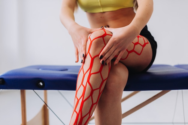 Молодая спортивная спортсменка, держа ее травмированную ногу после лечения кинезио лентой.