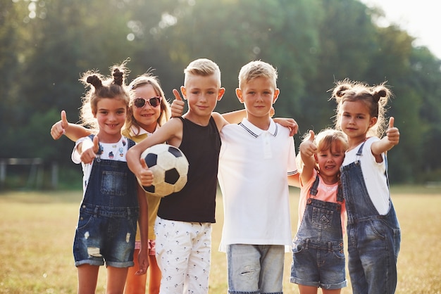 Young sportive kids with soccer ball stands together in the field at sunny day.