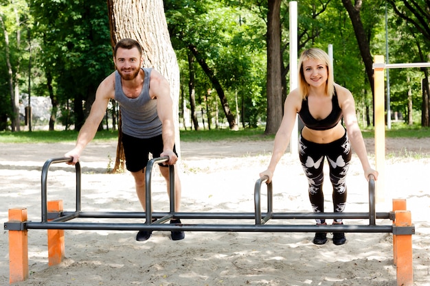 Young sportive woman and bearded man doing push-ups exercises in a parrk.