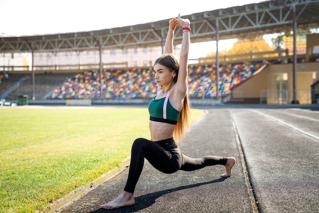 Young sportive woman making morning exercises outdoors on the stadium