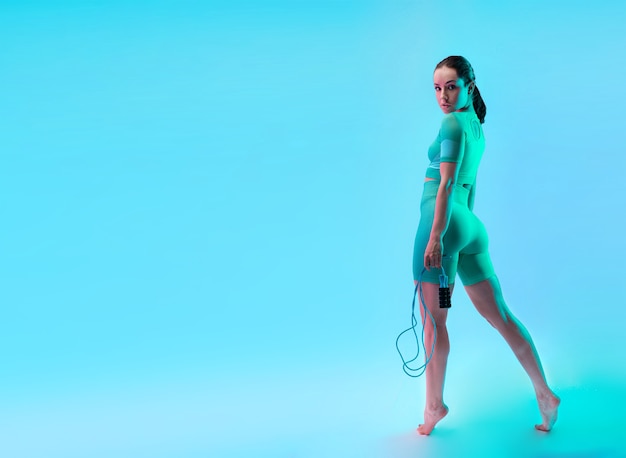 Young sportive woman training with skipping rope isolated on gradient studio background in neon light