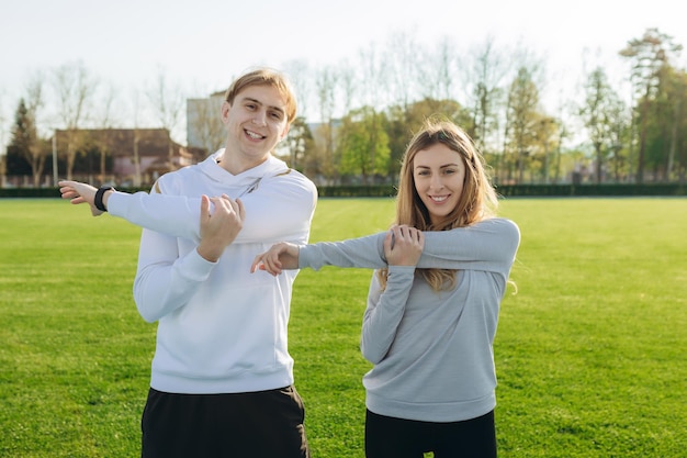 Young sports couple trains at the stadium in summer Doing various stretching exercises Fitness The concept of a healthy lifestyle