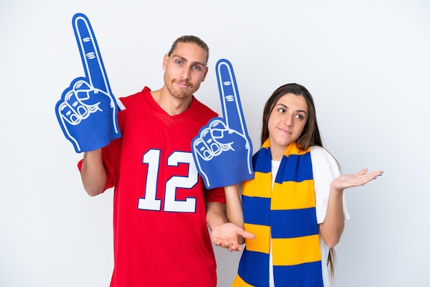 Young sports fan couple isolated on white background having doubts while raising hands and shoulders