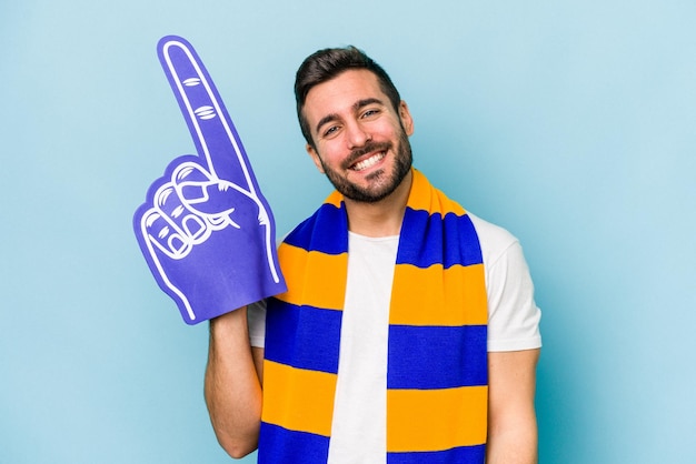 Young sports fan man isolated on blue background happy smiling and cheerful