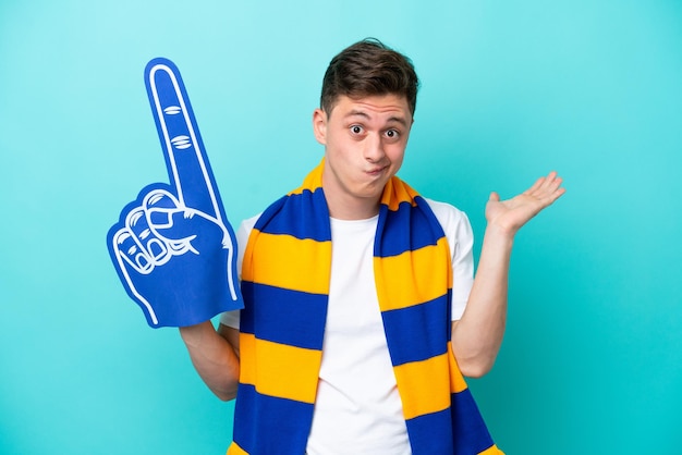 Young sports fan man isolated on blue background having doubts while raising hands