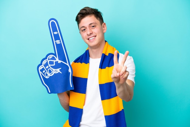 Young sports fan man isolated on blue background smiling and showing victory sign