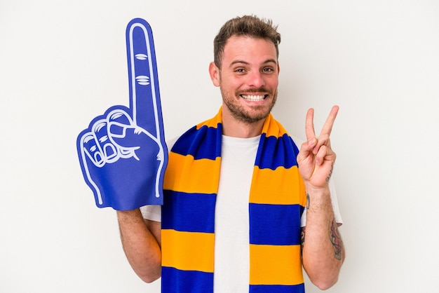 Young sports fan man isolated on white background joyful and carefree showing a peace symbol with fingers.