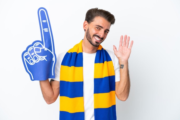 Young sports fan man isolated on white background saluting with hand with happy expression