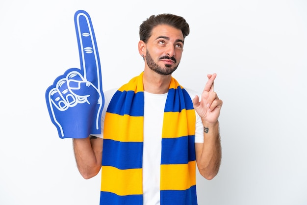 Young sports fan man isolated on white background with fingers crossing and wishing the best