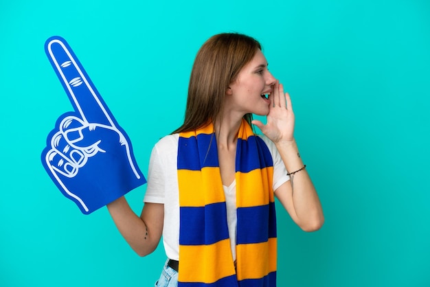 Young sports fan woman isolated on blue background shouting with mouth wide open to the side