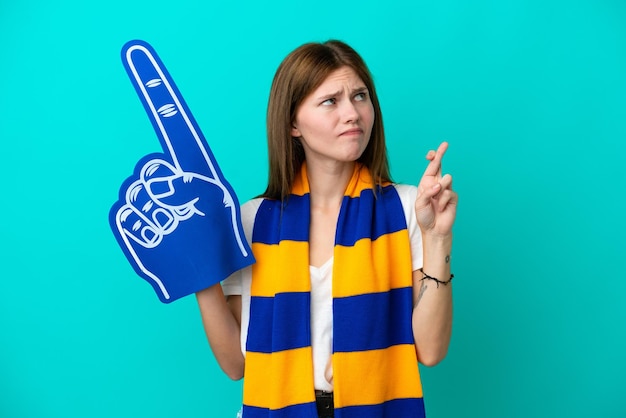 Young sports fan woman isolated on blue background with fingers crossing and wishing the best