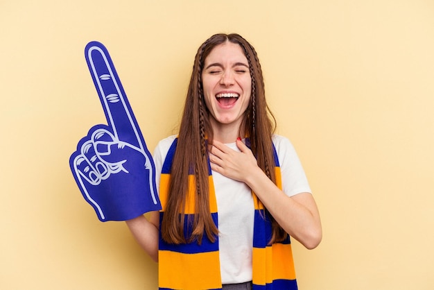 Young sports fan woman isolated on yellow background laughs out loudly keeping hand on chest.