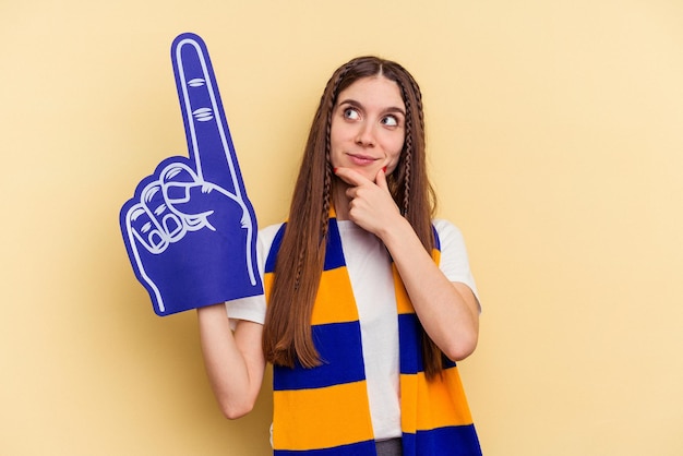 Young sports fan woman isolated on yellow background looking sideways with doubtful and skeptical expression.