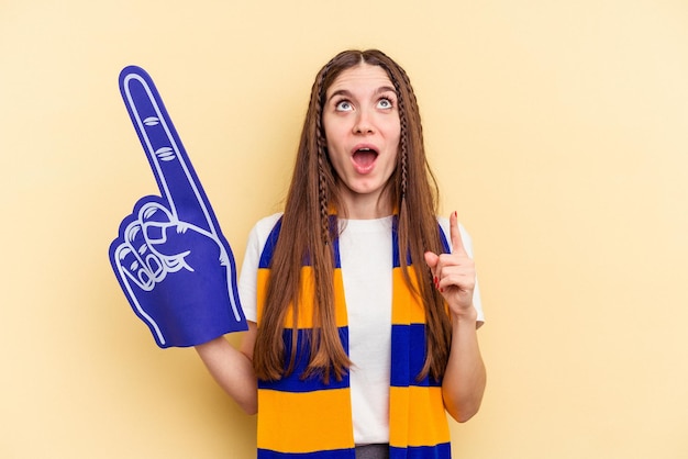 Young sports fan woman isolated on yellow background pointing upside with opened mouth