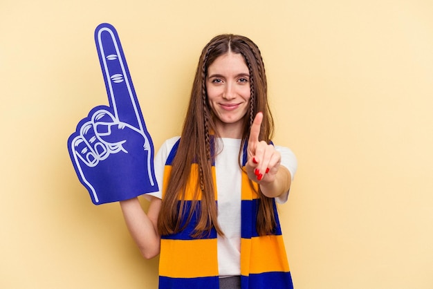 Giovane donna appassionata di sport isolata su sfondo giallo che mostra il numero uno con il dito