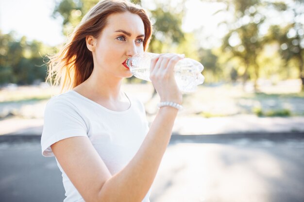 Foto giovane ragazza sportiva, acqua potabile dalla bottiglia, dopo un duro allenamento.