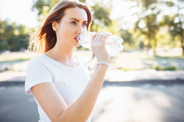 Photo young sports girl, drinking water from the bottle, after a hard workout.