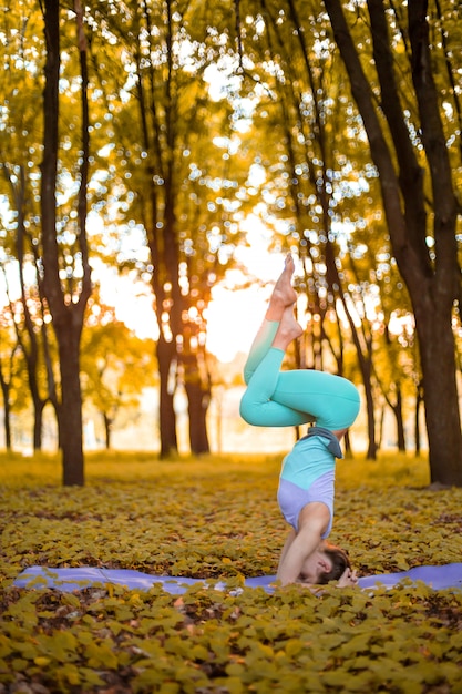 A young sports girl practices yoga in a quiet green forest in autumn at sunset, in a yoga asana pose. Meditation and oneness with nature