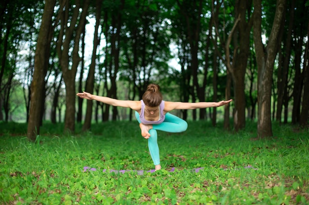 A young sports girl practices yoga in a quit green summer forest, yoga assans posture. 