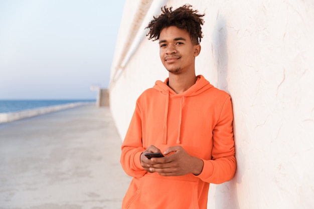 Ragazzo giovane sportivo all'aperto sulla spiaggia utilizzando il telefono cellulare