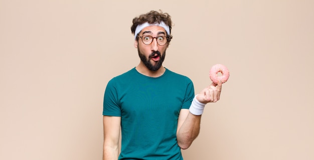 Молодой спортивный человек с закуской держит розовый сахарный пончик