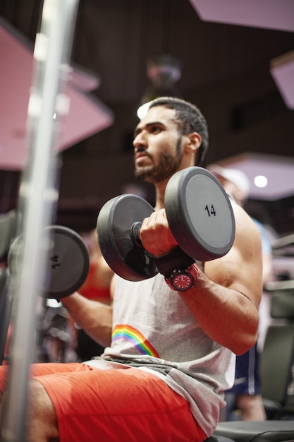 Young sports man performs exercises with dumbbells in the gym Young man in sportswear is training in the gym