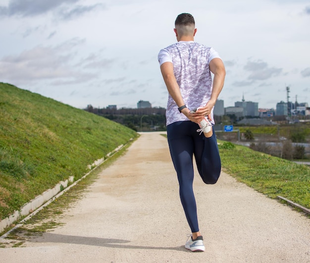 Young sports man stretching his leg before going for a run in green park outdoors