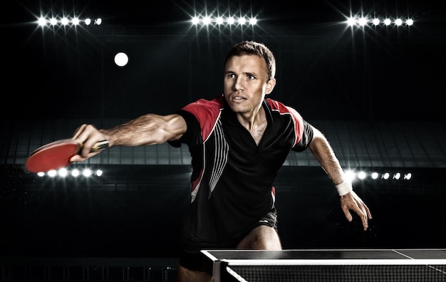 Young sports man tennisplayer in play on black background Action shot