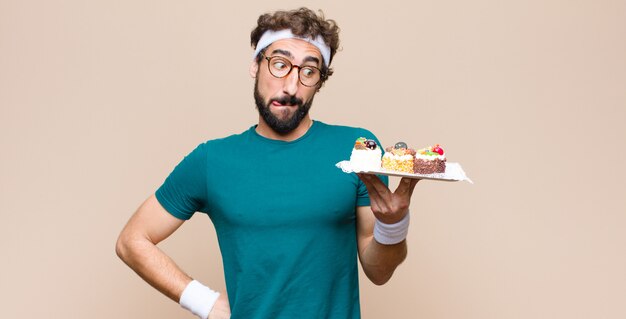 Young sports man with cakes against flat wall