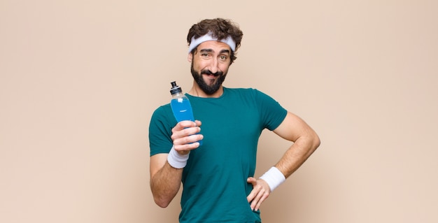 Young sports man with an energy drink bottle against flat wall