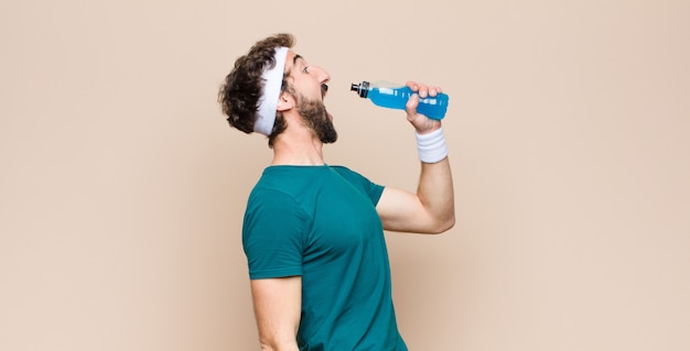 Young sports man with an energy drink bottle against flat wall