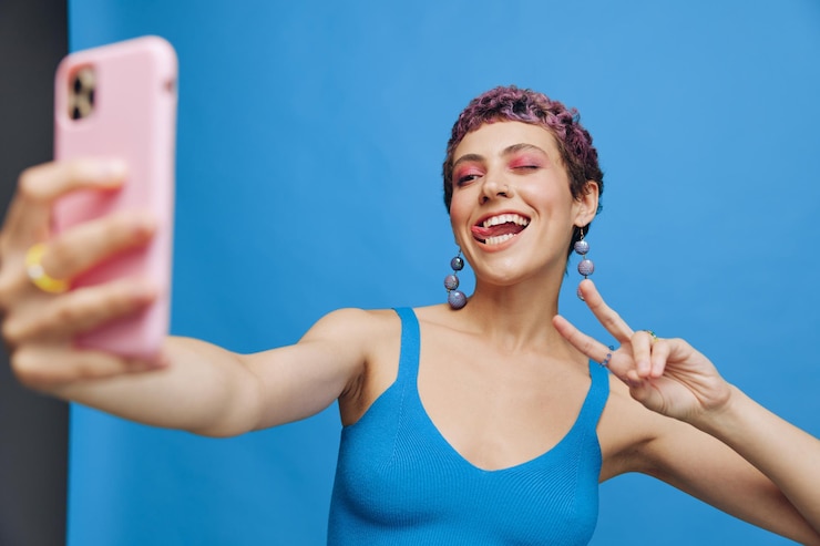 Photo young sports woman fashion blogger takes a picture of herself on the phone in blue sportswear smiling and showing her tongue on a blue monochrome background