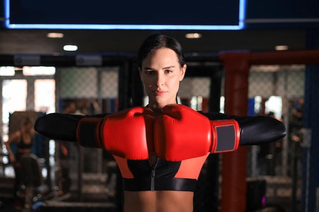 Young sports woman in tracksuit and putting hands together in red boxing gloves