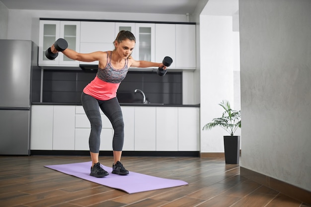 Young sports woman training shoulders at home using dumbbells