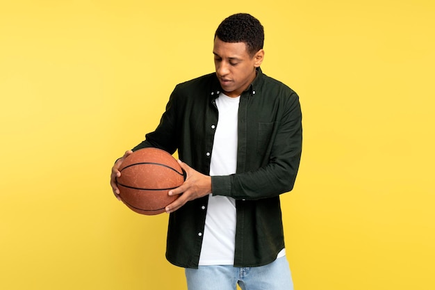 Young sportsman holding basketball ball and looking on it while standing