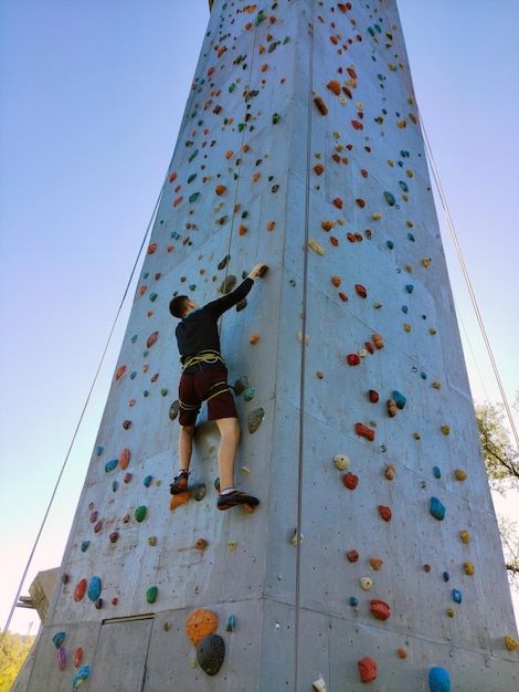 Молодой спортсмен поднимается по тренировочной стене для скалолазания Вид снизу