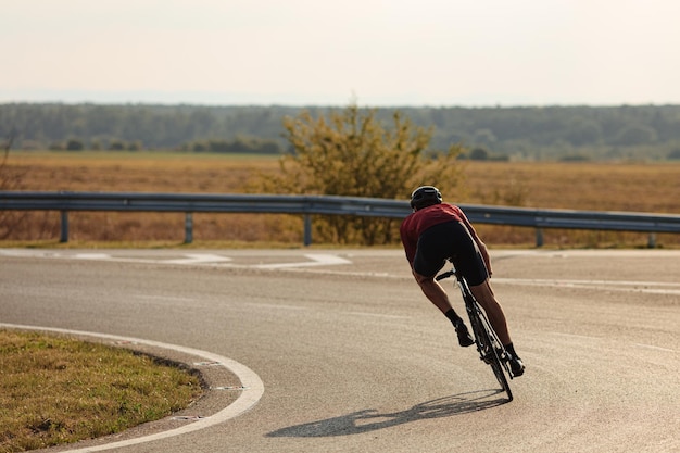 Photo young sportsman in protective helmet cycling with high speed on paved road morning sun