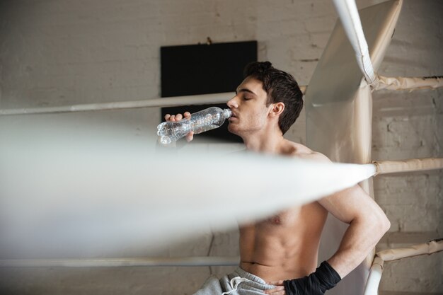 Young sportsman sitting in the ring and drinking