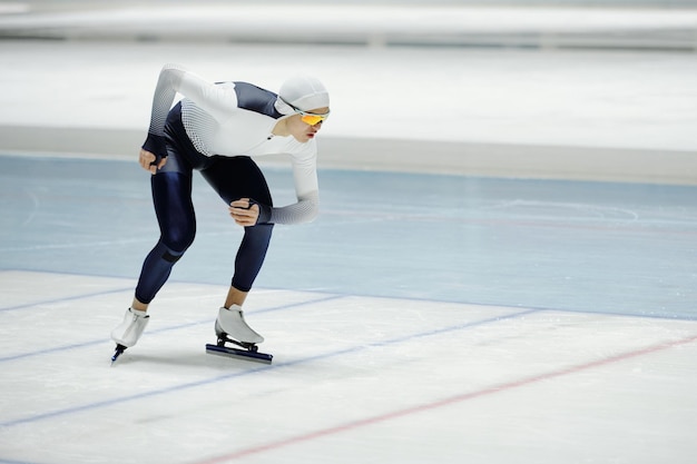 Young sportsman in speed skating uniform and eyeglasses sliding on ice rink