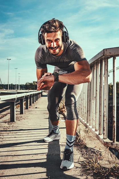 Young sportsman with headphones starts stopwatch before training at the bridge. He is preparing for jogging.