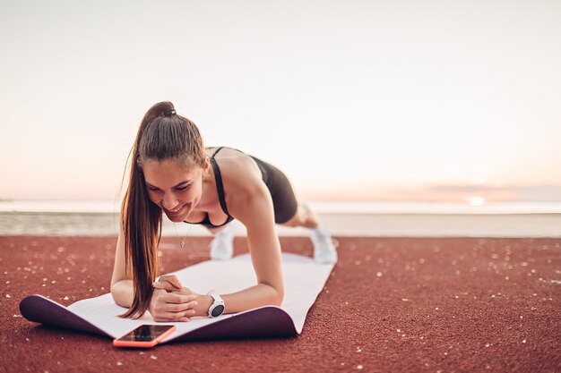 Young sportswoman doing exercise in plank position on the beach