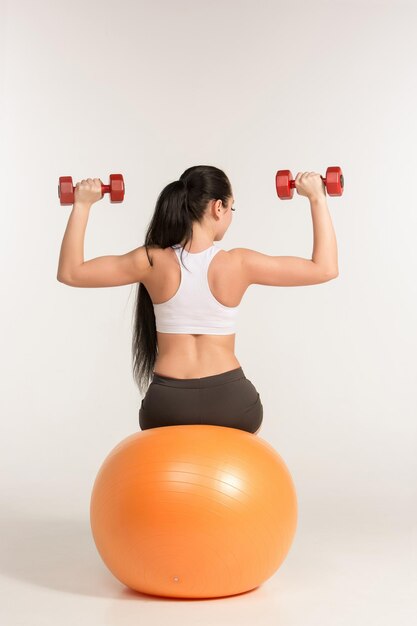 Young sportswoman doing fitness exercise with dumbbells on pilates ball