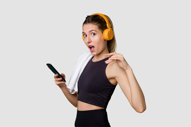 Молодая спортсменка, слушающая музыку, мотивированная и сосредоточенная, держащая телефон