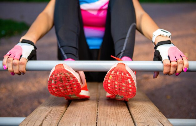 Young sportswoman in orange sneakers training at wooden park bench on summer morning