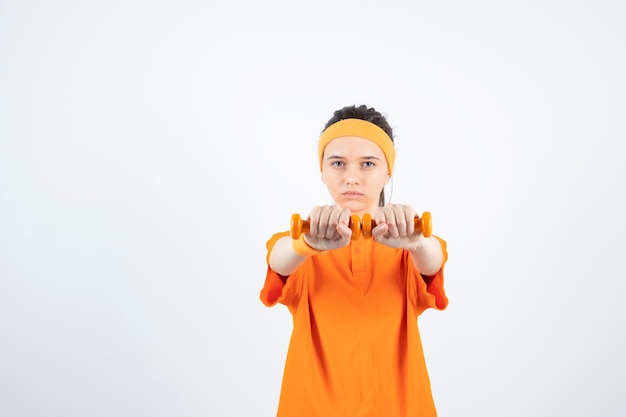 young sportswoman in orange t-shirt training with dumbbells.