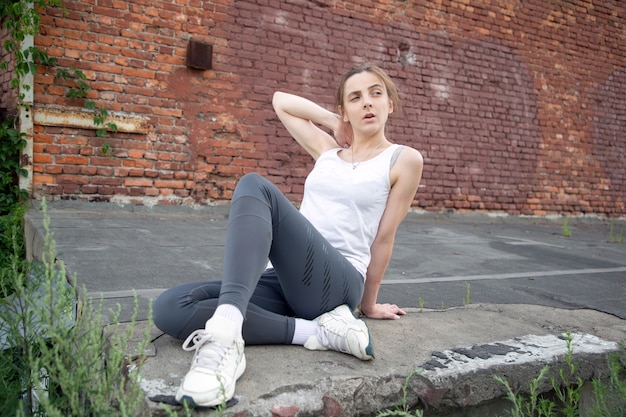 Young sportswoman sitting posing against the background of a red wall