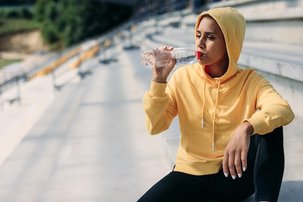 Young sporty brunette sitting on stairs and drinking water